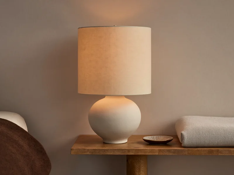 Keramik-Tischlampe mit cremefarbenem Leinenschirm auf einer Nachtkonsole neben einer Decke