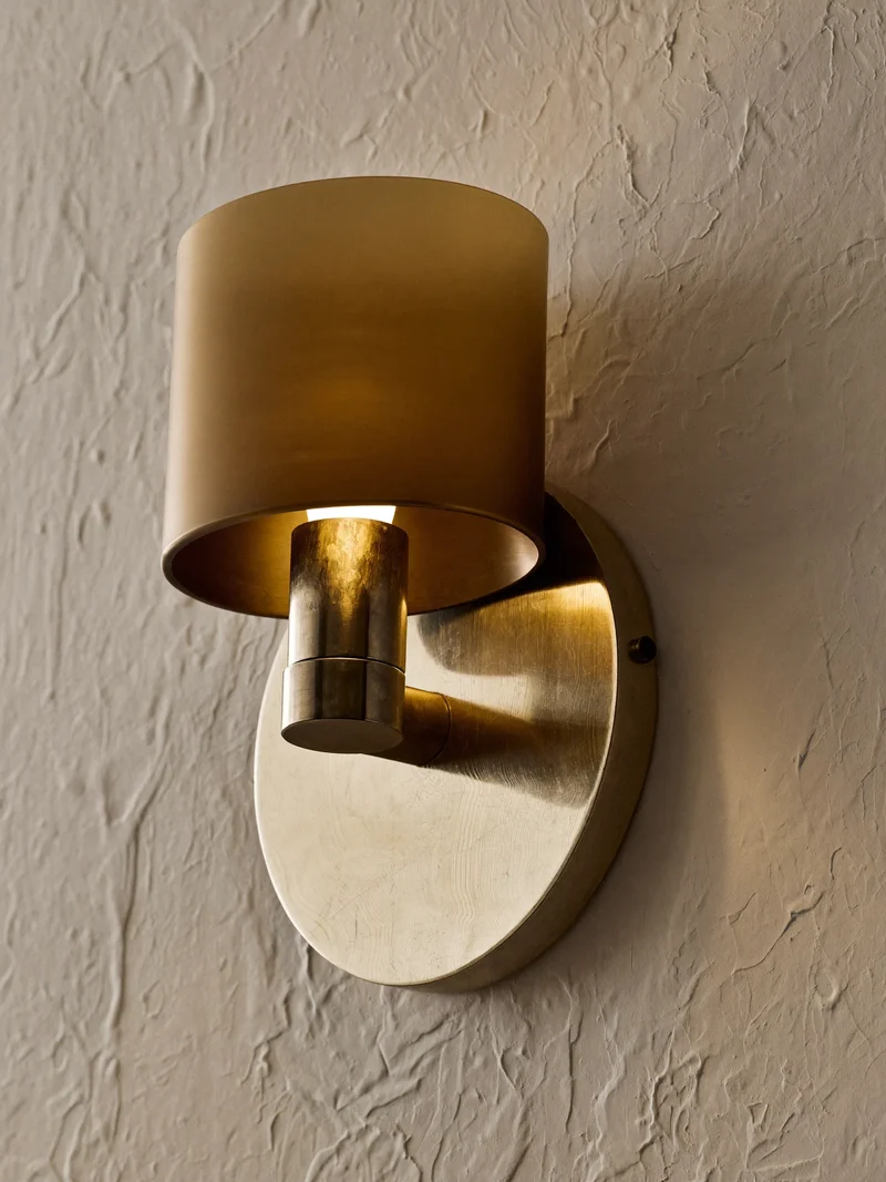 Verstellbare Wandleuchte mit warmem Metallarm an einer strukturierten Putzwand